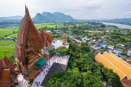 Kanchanaburi, Thailand-October 23, 2022 : Aerial view of Asian tourists at Wat Tham Seua, beautiful and ancient big golden Buddha image, rural villages and rice fields, mountains and blue sky background.の写真素材