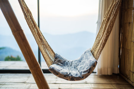 classic outdoor bed swing with cushions, wooden terrace with wicker swing with blurry nature background.の写真素材