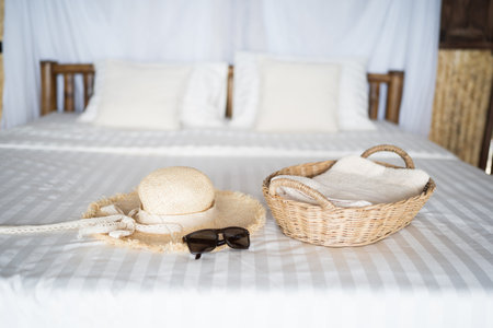 bedroom with wooden furniture and white bedclothes, wooden basket for towels, Hat and sunglasses.の写真素材