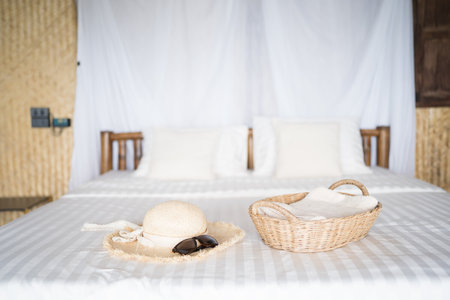 bedroom with wooden furniture and white bedclothes, wooden basket for towels, Hat and sunglasses.の写真素材