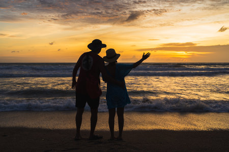 Asian tourist couple taking pictures of sunset at the beach, Beautiful sunset above sea, Colorful Orange and golden sunset sky, acation travel holiday concept.の写真素材