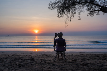 women sit on a chair on the beach with beautiful sea and sunrise sky, 
Outdoor lifestyle concept.の写真素材