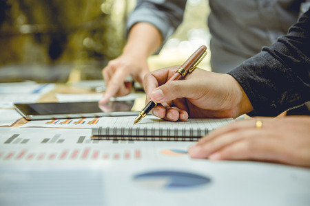 hand of businessman holding a pen and writing note book. There is his partner worker advising beside him.の写真素材