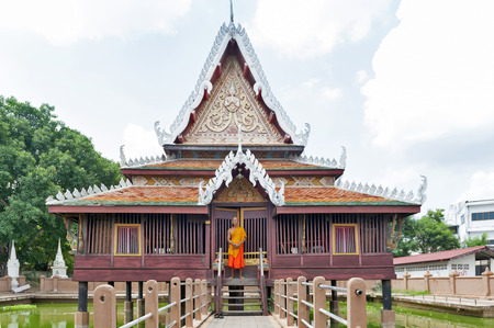 Yasothon, Thailand - May 2017: Thai Buddhist monk standing in front of Ho Trai - Traditional Thai-style building used as a library that houses Buddhist scriptures (Tripitaka or Pali Canon) located at Wat Mahathat Temple in downtown Yasothon, northeastern のeditorial素材