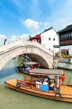 Shanghai, China - September 2019: Tourist wooden rowboat cruising pass an old stone bridge lies over a canal in Zhujiajiao Ancient Water Town, a historic village located in the Qingpu District of Shanghai, Chinaのeditorial素材
