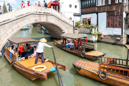 Shanghai, China - September 2019: Tourist wooden rowboat cruising pass an old stone bridge lies over a canal in Zhujiajiao Ancient Water Town, a historic village located in the Qingpu District of Shanghai, Chinaのeditorial素材