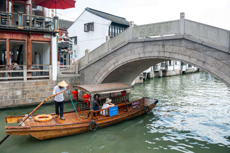 Shanghai, China - September 2019: Tourist wooden rowboat cruising pass an old stone bridge lies over a canal in Zhujiajiao Ancient Water Town, a historic village located in the Qingpu District of Shanghai, Chinaのeditorial素材