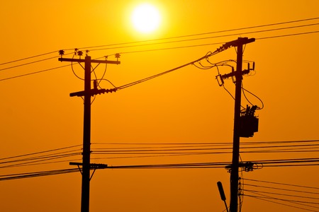 Silhouette of electric pole power lines and wires in sunset skyの写真素材