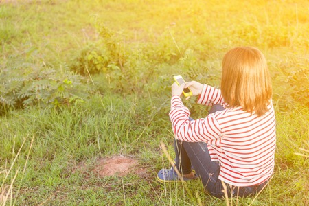 Portrait of happy young woman sitting on grass and using smart phone