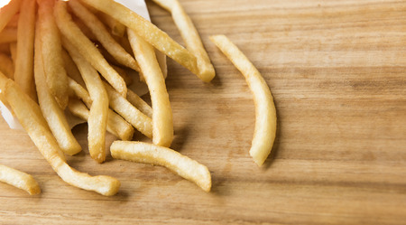 french fries in a little white paper bag on wood board