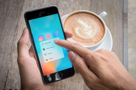 CHIANG MAI, THAILAND - JULY 7,2016: A women holds Apple iPhone 6S with Instagram application on the screen with latte hot, coffee cup on wood desk. Instagram is a photo-sharing app for smartphones.のeditorial素材