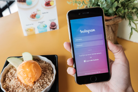 CHIANG MAI, THAILAND - JAN 7, 2017: A woman holds Apple iPhone 6S with Instagram application on the screen with cheese ice Cream on Yellow table. Instagram is a photo-sharing app for smartphones.のeditorial素材