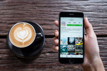 CHIANG MAI, THAILAND - OCT 24,2016: A women holds Apple iPhone 6S with Instagram application on the screen with latte hot, coffee cup on wood desk in coffee shop. Instagram is a photo-sharing app for smartphones.のeditorial素材