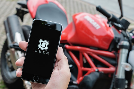 CHIANG MAI,THAILAND - Aug 27,2016 : A MAN hand holding Uber app showing on iphone 6s with background Ducati motorcycle. Uber is smartphone app-based transportation networkのeditorial素材