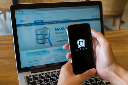 CHIANG MAI,THAILAND - Aug 4,2016 : A MAN hand holding Uber app showing on iphone 6s or 6s Plus background  Mysql in laptop. Uber is smartphone app-based transportation networkのeditorial素材