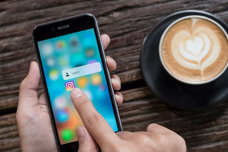 CHIANG MAI, THAILAND - OCT 24,2016: A women holds Apple iPhone 6S with Instagram application on the screen with latte hot, coffee cup on wood desk in coffee shop. Instagram is a photo-sharing app for smartphones.のeditorial素材
