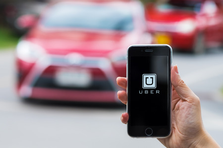 CHIANG MAI,THAILAND - JUL 24,2016 : A MAN hand holding Uber app showing on iphone 6s on road and red car. Uber is smartphone app-based transportation networkのeditorial素材
