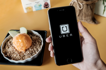 CHIANG MAI,THAILAND - JAN 7,2016 : A MAN hand holding Uber app showing on iphone 6s with  cheese ice Cream on yellow table . Uber is smartphone app-based transportation networkのeditorial素材