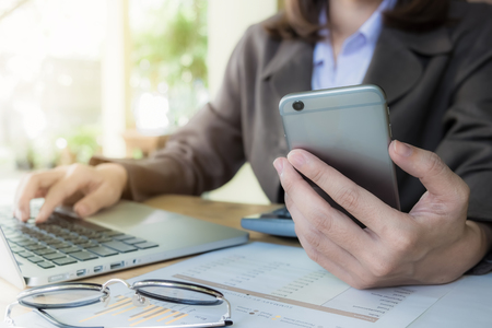 Business woman hand holding smartphone and using laptop computer for work in office.の写真素材