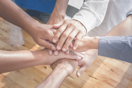 Group of people putting their hands working together on wooden background in office. group support...