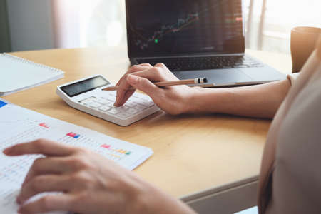 Business woman using calculator and computer to trade charts to find buy and sell points for her...