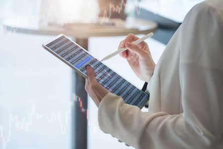 Business woman using tablet to trade charts to find buy and sell points for her port.の写真素材