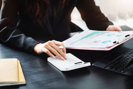 Business woman using calculator to review balance sheet annual using document and laptop computer to calculating budget. audit and Check integrity before investment conceptの写真素材