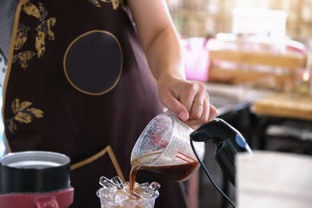 A female employee pours coffee into a plastic cup for customersの写真素材