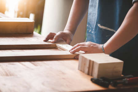 A carpenter measures the planks to assemble the parts, and build a wooden table for the customer.の写真素材
