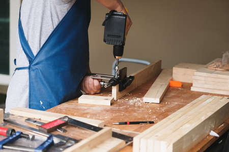 Woodworking entrepreneurs are using a drill through the wood holes to assemble and build wooden tables for customers.の写真素材