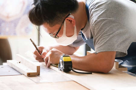 A carpenter measures the planks to assemble the parts and build a wooden table for the customer