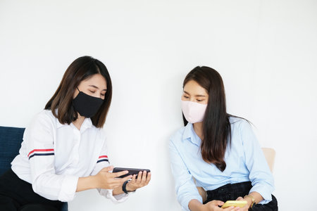 social distancing concept, Two women wearing masks and distancing while sitting on mobile phones following virus social trend.の写真素材
