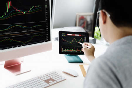 Investment professionals point their pen at their computer monitor to analyze the stock market for...