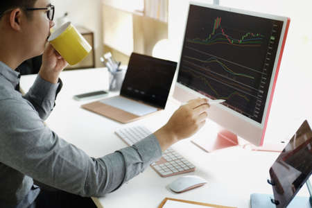 Investment professionals point their pen at their computer monitor to analyze the stock market for...