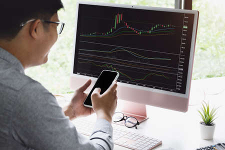New normal, self-employed man are using mobile phone and computer laptop to trade stocks for profit, buying and selling.の写真素材