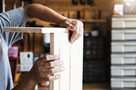 A carpenter measures the planks to assemble the parts, and build a wooden table for the customer.