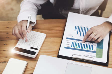 Business woman using calculator to review balance sheet annual using document and laptop computer to...