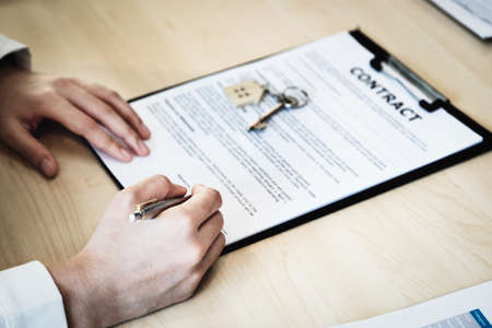 The customer is holding a pen and is reading the housing purchase contract before signing it.
