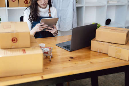 Work from home. happy women selling products online Start a small business owner by using tablet and laptop computer to calculate prices and prepare for postage.の写真素材