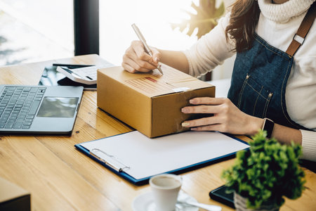 Business owners use pens to write on parcel boxes and use computers to check online orders to prepare packaged boxes. Pack products for delivery to customers.の写真素材