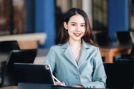 A female entrepreneur or businesswoman showing a smiling face while operating a computer tablet...