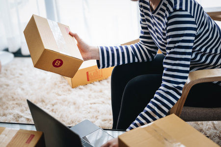 Online merchandising business idea, beautiful girl holding a parcel delivery box and using a computer to input Track And Trace parcel numbers to customers.の写真素材