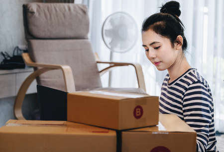 Online merchandising business idea, a beautiful girl is using a computer to insert Track And Trace parcel numbers to customers.の写真素材