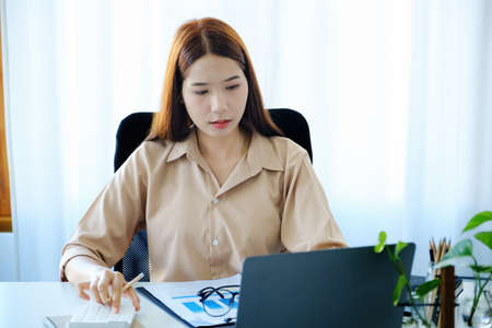 A young woman uses computers and calculators to work from home to avoid the risk of contracting the...