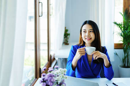 Manager, entrepreneur, female employee sitting and drinking coffee expressing a smiling face while taking a break from hard work.の写真素材
