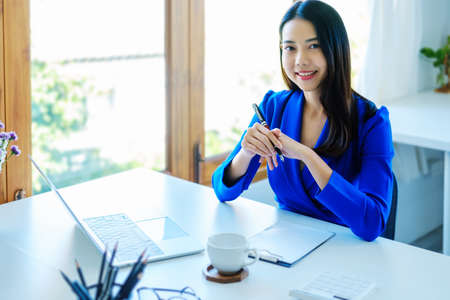 An Asian entrepreneur or businesswoman shows a smiling face while working with using computer on a wooden table.の写真素材