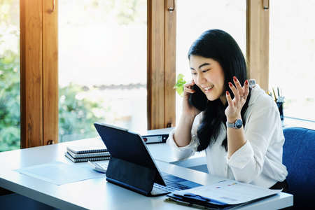 A female entrepreneur or businesswoman shows a smiling face while using smartphone and tablet computer for video conference working on a wooden table.の写真素材
