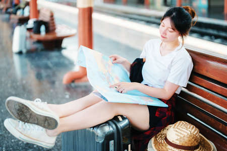 summer, relax, vacation, travel, portrait of a cute Asian girl looking at a map to plan a trip while waiting at the train stationの写真素材