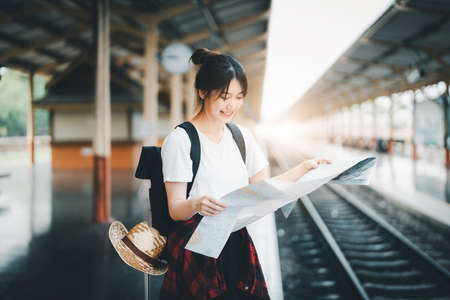 summer, relax, vacation, travel, portrait of a cute Asian girl looking at a map to plan a trip while waiting at the train stationの写真素材