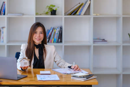 Asian woman accountant, business woman, real estate agent, holding a pen, pointing at home loan and...